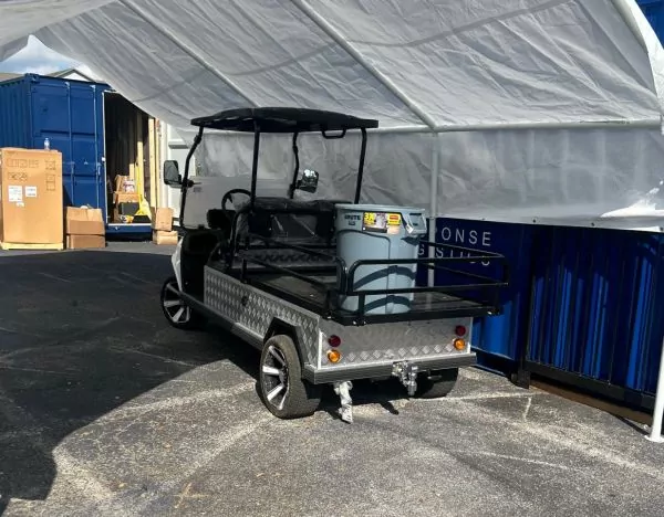 Black utility golf cart with diamond-plate aluminum cargo bed at outdoor work and event venue — versatile cargo hauling for events and service operations